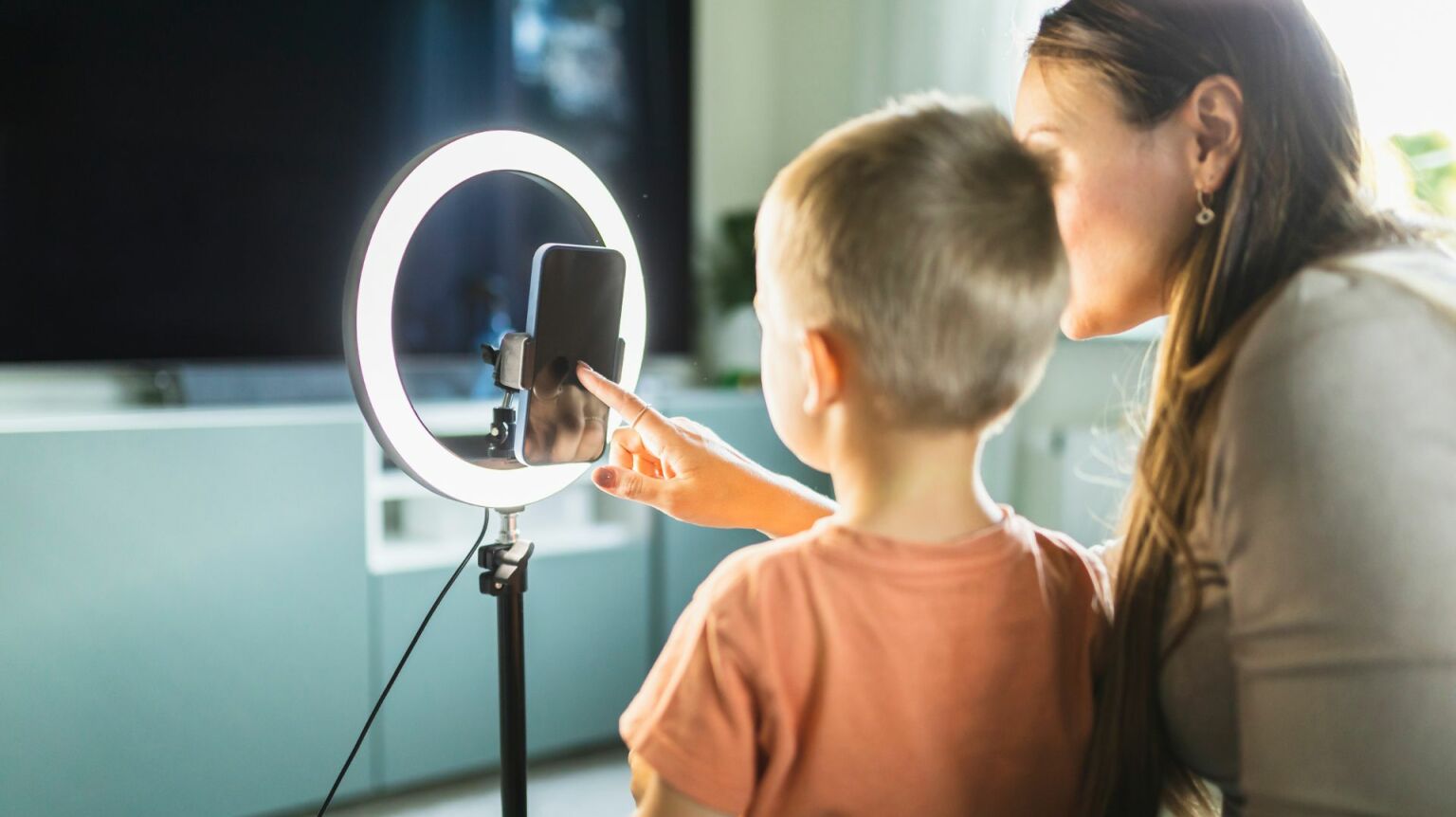 Mother live streaming with son on smart phone with ring light at home.