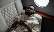 Person lying in airplane chair with headphones on and eyes closed.