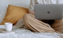 Person sitting on a bed on their laptop.