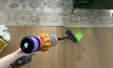 Person holding Dyson V12 Detect Slim to clean hardwood floor with laser on