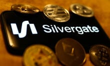 Silvergate logo displayed on a phone screen, surrounded by coins representing cryptocurrencies.