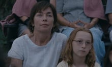 A woman in a white t-shirt and a young girl in glasses sit together on the grass.