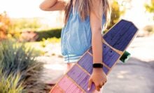 A young girl hold a longboard and wears a Fitbit