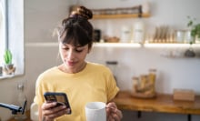 A woman looks at her phone in the kitchen.