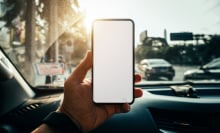 A hand holding an iPhone over a car dashboard.