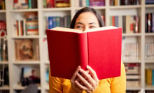 A woman poses with a book in front of a book shelf