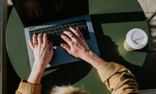 Woman typing on Mac on green table with coffee cup