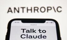 Anthropic Claude website displayed on a phone screen and Anthropic logo displayed on a screen in the background