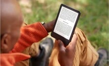 a person reads on a kindle e-reader while sitting on the ground outside