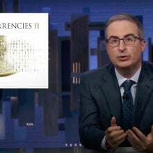 A man in glasses and a suit sits behind a desk, looking at the camera, next to an image of a coin that read "cryptocurrency".