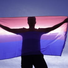 adult man on his back with bisexual flag on a sunny day