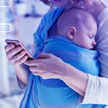 Mom looks at her phone while carrying her baby in a sling.