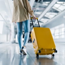 A woman in denim jeans rolling a bright yellow suitcase through an airport. 