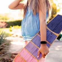 A young girl hold a longboard and wears a Fitbit