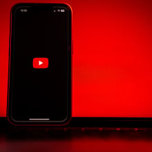 A phone showing the YouTube logo stands propped in front of a glowing red laptop.