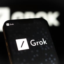 A phone displaying the Grok xAI logo, which is a white box with a black slash across it. 