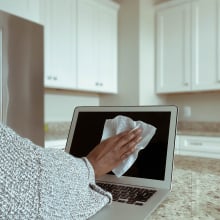 Close-up of unrecognizable woman in kitchen cleaning laptop screen with disinfectant wipe