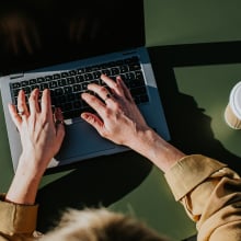 Woman typing on Mac on green table with coffee cup