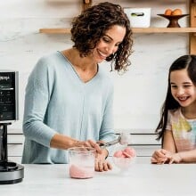 a mom makes ice cream with the ninja creami machine while daughter looks on smiling