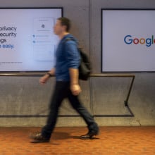 A person walks in front of a screen with the Google logo, and another with a Google privacy slogan