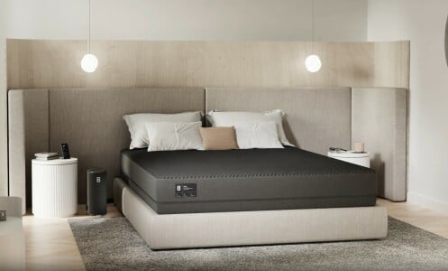 a bed sits in the center of a bedroom with the Eight Sleep Pod 3 cover over the mattress and pillows above the cover