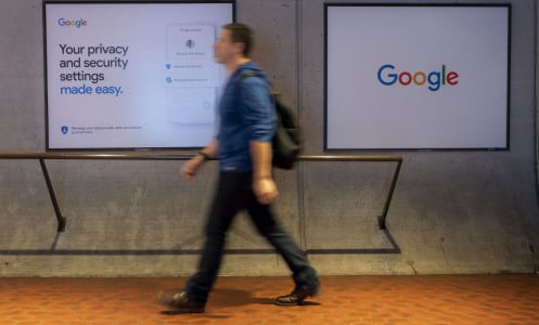 A person walks in front of a screen with the Google logo, and another with a Google privacy slogan