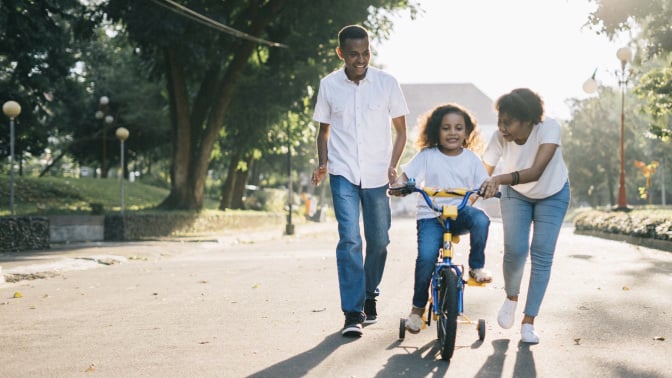 parents teaching kid how to ride a bike in the street