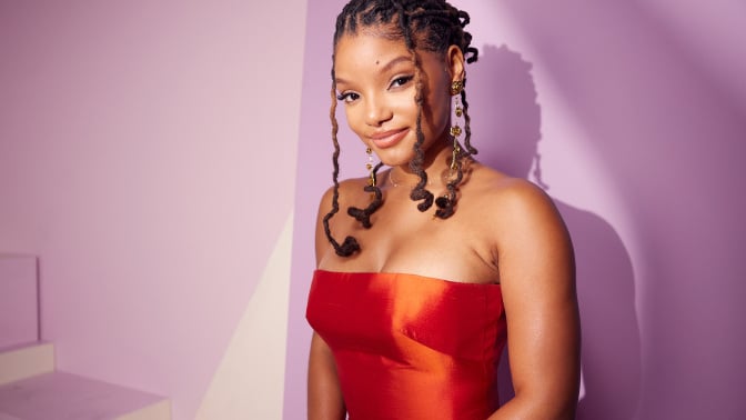 Halle Bailey wearing a red dress in front of a pink background