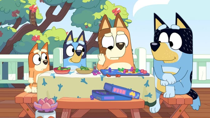 A family of cartoon dogs sit around a table outside.