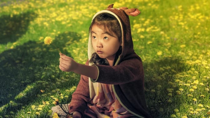 A young girl sits on a field of a grass while four shadows loom over her. 