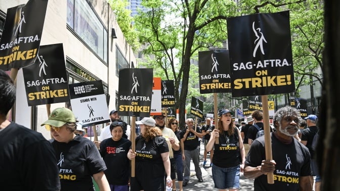 A group of striking people in black shirts holding signs that say "SAG-AFTRA on strike!" walk the streets of New York.