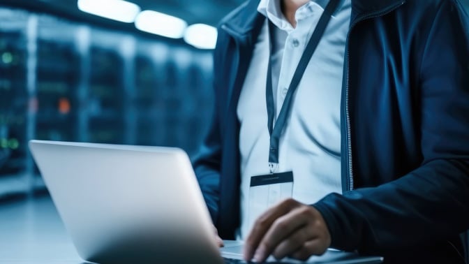 Man working on laptop in server farm.