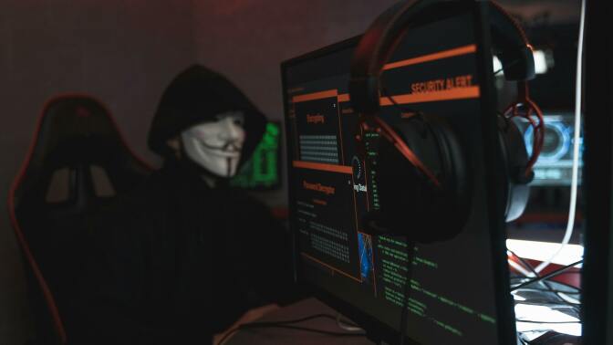 Hacker in guy fawkes mask by computer displays