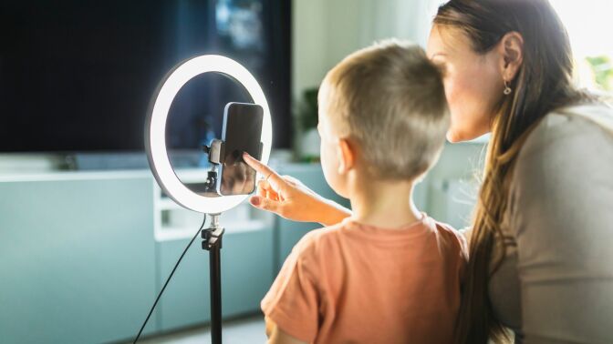 Mother live streaming with son on smart phone with ring light at home.