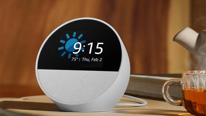 the amazon echo spot shows the time while sitting on a table with a cup of tea beside it