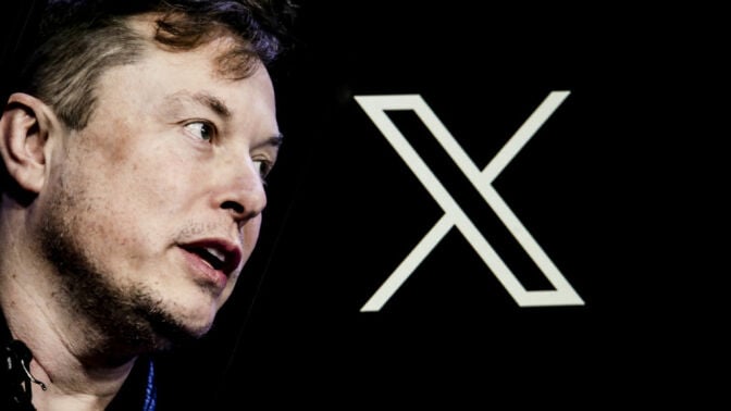 Elon Musk's photo is displayed on a phone screen in front of a computer screen displaying. the Twitter/X logo.