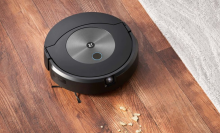 Roomba robot vacuum cleaning crumbs on hardwood floor with rug in peripheral