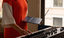 a woman holding an m2 apple macbook air in one hand while playing a keyboard with the other