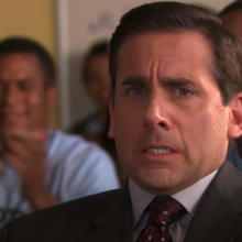 A man (Steve Carell as Michael Scott on "The Office") sitting at a desk in a classroom surrounded by high school students.