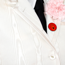 A zoomed-in photo of Phoebe Bridgers' white suit lapel, with a pink flower and a red "ceasefire now" button pinned to it.