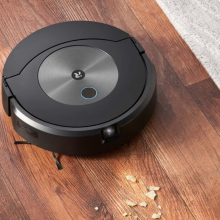 Roomba robot vacuum cleaning crumbs on hardwood floor with rug in peripheral