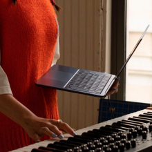 a woman holding an m2 apple macbook air in one hand while playing a keyboard with the other