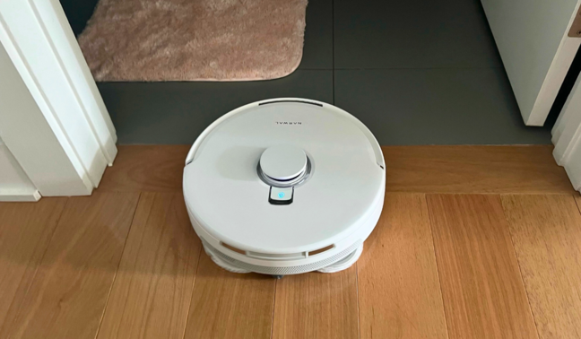 Narwal robot vacuum mopping hardwood floor approaching doorway of bathroom with tile floor